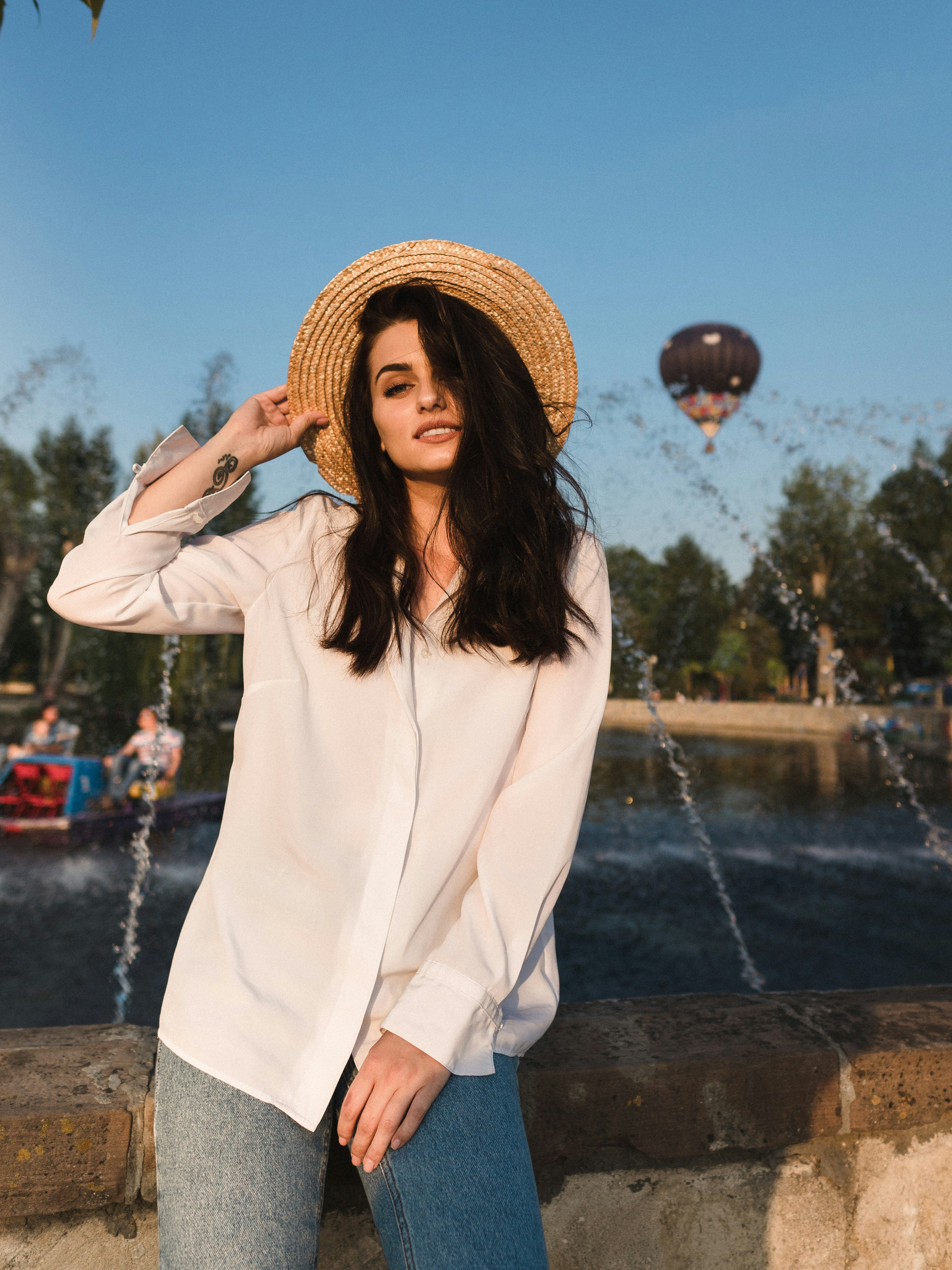 woman in white long sleeve shirt and brown straw hat standing on gray concrete floor during